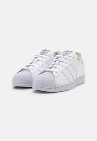 Vita sneakers med en texturerad gummitåhätta, slät läderöverdel, tre sidostripes och ljusblå branding på tungan.