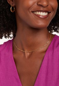 Gouden ketting met een gedraaide ontwerp, gedragen met een levendig roze top. Heeft kleine schakels en een gladde textuur, die de huidskleur aanvult.
