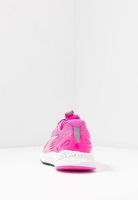 Scarpa sportiva rosa con tomaia in rete, colletto imbottito e dettagli riflettenti. Presenta una suola intermedia bianca con dettagli testurizzati e una suola in gomma.