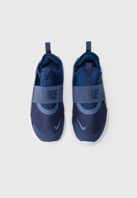 Baskets slip-on Nike bleues avec un dessus en maille, une sangle élastique et une semelle blanche. Présente des textures contrastantes et le logo Nike sur la sangle.