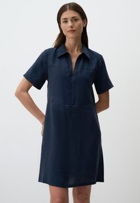 Robe bleu marine en tissu lisse, avec une fermeture à glissière sur le devant, des manches courtes et une coupe décontractée dotée de deux poches avant.
