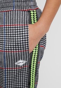 Geruite joggerbroek met zwart, rood en blauw patroon, voorzien van een neon groene streep, elastische tailleband en een zijzak met logo.