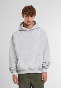 Sivá mikina vyrobená z teplákovine, s veľkou prednou kapsou, kapucňou na šnúrku a ribovanými manžetami. Jednoduchý, uvoľnený strih.