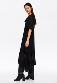 Mustahdusha musta mwega yenye mikono mifupi, iliyoandaliwa na nyenzo za uwazi kwenye mguu. Jozi ya viatu vya sole na kisigino cheusi inakamilisha mavazi hayo.