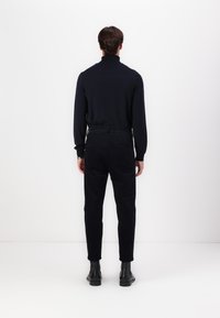 Black turtleneck sweater paired with dark trousers and leather boots. Smooth fabric, fitted design, with a simple and clean silhouette.