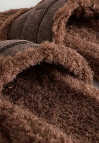 Chaussons en peluche brun avec un extérieur doux et texturé. Dotés d'une doublure moelleuse et d'un design simple pour le confort et la chaleur.