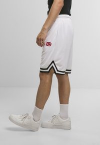 Hvide sports shorts med sort kant og et rødt logo. Stoffet er let og åndbart, med en afslappet pasform.
