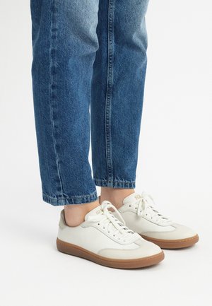 Białe skórzane sneakersy z teksturowaną powierzchnią, sznurowanym designem i gumową podeszwą; zestawione z podkręconymi niebieskimi dżinsami.