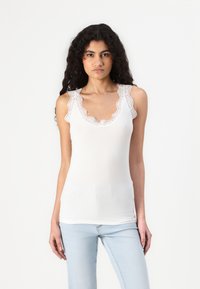 White ribbed tank top with lace trim along the neckline and armholes; fitted design, soft texture, and scalloped edges.
