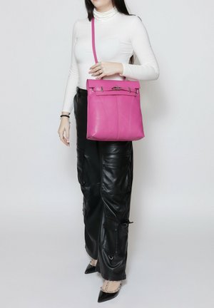 Sac à main en cuir rose avec une forme structurée, fermeture supérieure, accents en métal argenté et une longue sangle réglable pour un port croisé.