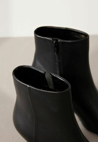 Mustad mustasir boots, mis on valmistatud siledast nahast, funktsioneerivad külgpedi ja ümarate tipudega. Disain on stiilne ja minimalistlik siluett.