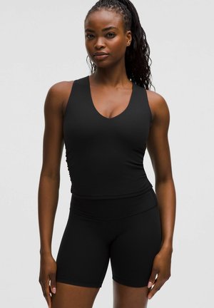 Zwarte sportieve tanktop met een V-hals en ribbelstructuur, gecombineerd met bijpassende hoge shorts. Beide zijn aansluitend en naadloos.