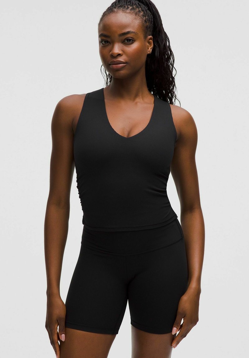 Zwarte sportieve tanktop met een V-hals en ribbelstructuur, gecombineerd met bijpassende hoge shorts. Beide zijn aansluitend en naadloos.