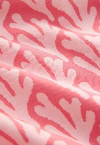 Tissu rose doux avec des motifs abstraits de cœur et de branches rouge corail, montrant la texture et de doux plis.