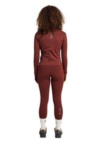 Mörkröd atletisk set som innehåller en åtsittande långärmad topp och leggings. Texturerat material med logotypdetaljer på ryggen och vänster ben.