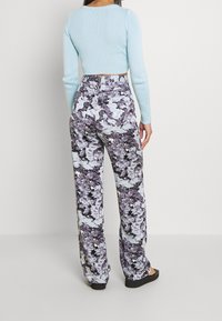 Jasnoniebieski, prążkowany, krótki sweter zestawiony z spodniami o wysokim stanem z kwiecistym wzorem w odcieniach fioletu i szarości, noszony z czarnymi sandałami.