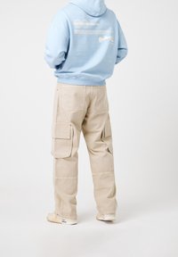 Jasnoniebieska bluza z kapturem z graficznymi detalami na plecach, zestawiona z beżowymi spodniami cargo z wieloma bocznymi kieszeniami i luźnym krojem.