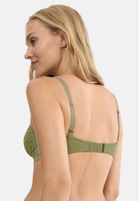 Zielony koronkowy biustonosz z gładkim pasem z tkaniny, regulowanymi ramiączkami i zapięciem na haftki z tyłu. Misterna koronka z wzorem.