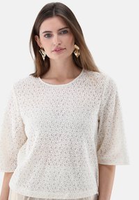 Weißes, strukturiertes Oberteil mit floralem Muster, rundem Ausschnitt und kurzen Ärmeln. Es zeichnet sich durch eine lockere Passform und weichen, leichten Stoff aus.