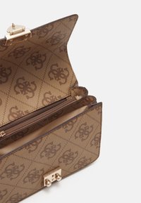 Sac à main marron à motifs ouvert montrant un compartiment intérieur zippé et un fermoir doré sur fond clair.