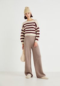 Gebreide trui met kastanjebruine strepen op beige, cropped ontwerp; brede geribbelde beige broek; beige gebreide muts; zachte stof; casual look.