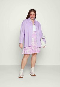 Camisa oversized lavanda, top cropped branco, saia ruffled rosa tie-dye, ténis brancos de cano alto e óculos de sol rosa claro.