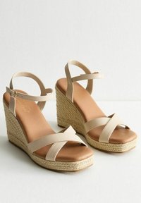 Sandales compensées beiges avec un design à lanières croisées, tige en simili cuir et semelle en jute. Semelle intérieure lisse avec un style à bout ouvert.