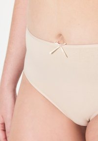 Beige hooggetailleerde slip van zachte stretchstof. Voorzien van een kleine satijnen lintaccent bij de tailleband voor detail.
