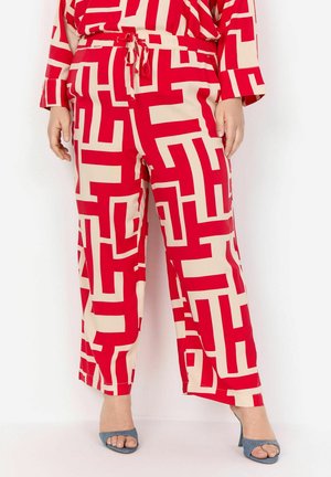 Red and beige patterned trousers with a geometric design, featuring an elastic waistband and relaxed fit, paired with blue open-toe heels.