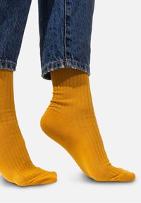 Żółte skarpetki w prążki, wykonane z miękkiego materiału, z zaokrąglonym czubkiem i długości do połowy łydki, noszone z niebieskimi dżinsami.