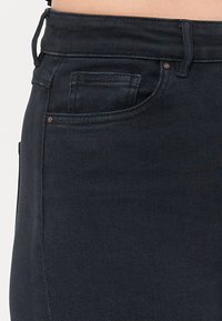 Tumed denim teksad, millel on esitasku, minimaalne õmblemine ja sile tekstuur. Kangas on kerge venivusega mugavuse tagamiseks.