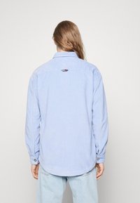 Jasnoniebieska sztruksowa koszula z kołnierzykiem zapinanym na guziki, długimi rękawami oraz metką z logo z tyłu, przy szyi. Materiał o teksturze z pionowymi prążkami.