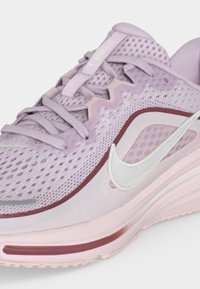 Ανοιχτό μωβ αθλητικό παπούτσι Nike με επάνω μέρος από διαπνέον διχτυωτό υλικό, λευκό λογότυπο Swoosh και μαξιλαρωμένη σόλα με λεπτομέρεια σε χρώμα βουργουνδί.