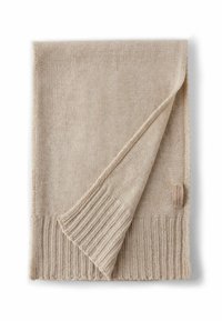 Écharpe en tricot beige avec des bords côtes. Texture douce, repliée avec une étiquette en tissu visible dans un coin.