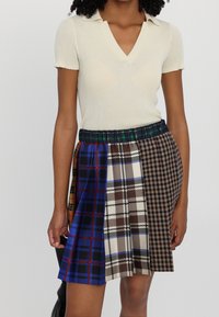 Falda de cuadros multicolor con una mezcla de patrones en marrón, azul y negro; cinturilla elástica y diseño plisado. Top de manga corta de canalé.