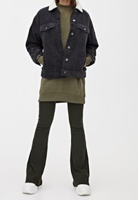 Mörk kordflorjacka med vit shearlingkrage, ihop med en olivgrön tunika och figursydda mörkgröna byxor, avslutat med vita sneakers.