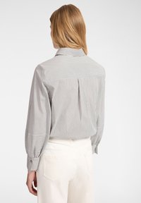 Blusa a righe in bianco e nero con collo classico, maniche lunghe e polsini con bottoni. Presenta una vestibilità ampia e dettagli con piega sul retro.