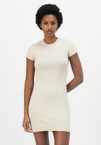 Beige fitted dress with short sleeves, crew neckline, and Calvin Klein logo on chest. Smooth texture with stretchy, form-fitting design.