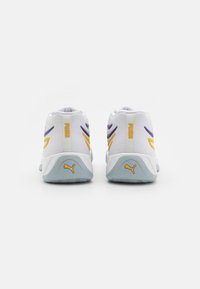Chaussures de sport blanches avec des accents violets et jaunes, en matériau mesh, talon arrondi et semelle texturée avec un petit logo à l'arrière.