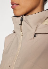 Chaqueta cremosa con cremallera y alto cuello, con un tejido texturizado, cremallera oculta y forro interior negro.