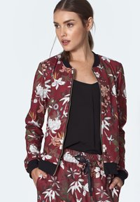 Bordowa bomberka w kwiaty z czarnymi ściągaczami przy mankietach i kołnierzu, zdobiona białymi i przytłumionymi zielonymi wzorami kwiatowymi, z zamkiem błyskawicznym i lekkim materiałem.