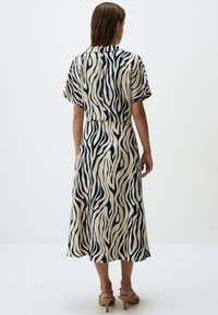 Robe beige à manches courtes, longueur genou, avec des rayures zèbre navy ; dotée d'un col et d'une coupe décontractée. Tissu lisse avec une texture subtile.
