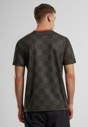 Grøn t-shirt med mønster, der har et ternet design i mørkere nuancer, korte ærmer og en kontrasterende orange halsudskæring.