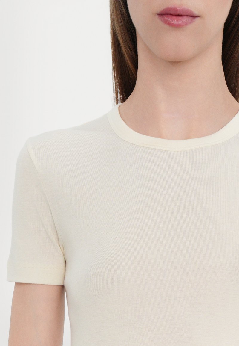 Camiseta de manga corta en color crema, hecha de una tela suave y ligera, con un cuello redondo sencillo y costuras limpias.