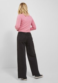 Pantaloni neri a gamba larga abbinati a un maglione aderente rosa. Il tessuto appare morbido, con una leggera trama e cuciture visibili. Sneakers nere completano il look.