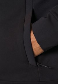 Felpa nera con tasca laterale, texture liscia e cordino regolabile all'orlo per personalizzare la vestibilità.