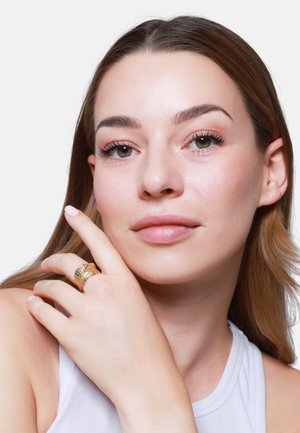 Goldring mit strukturierten Oberflächen und drei Bändern, getragen an einer Hand mit natürlichem Nagellack. Nahaufnahme eines Gesichts einer Person mit leichter Make-up.
