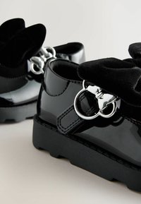 Schwarze Lacklederschuhe mit einer Samtschleife oben, silberner Hardware und einer massiven schwarzen Laufsohle. Mit gesteppten Details.