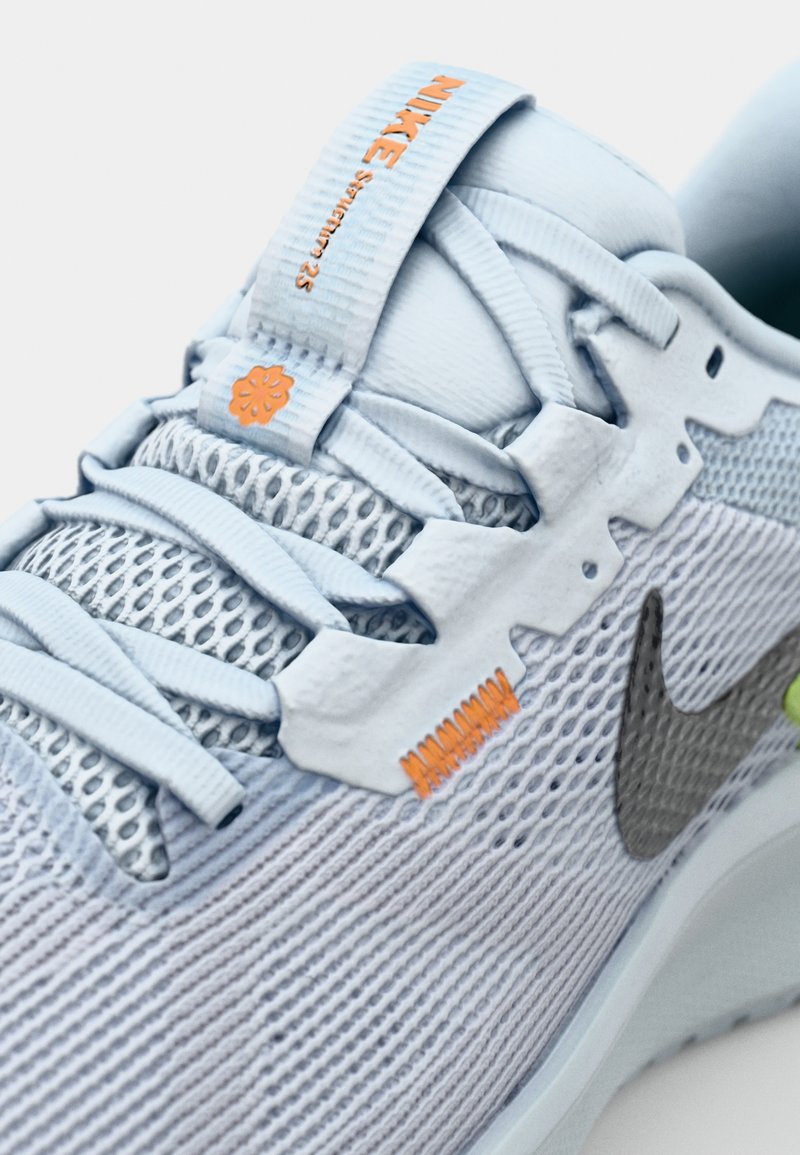 Helle blaue Sportschuhe mit einem Mesh-Obermaterial, reflektierendem grauen Nike-Logo, strukturierten Schnürsenkeln und orangefarbenen Akzenten an der Zunge und Zwischensohle.