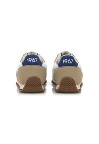 Scarpe sportive bianche e beige con un accento blu sul tallone che presenta il numero "1967" in bianco, suola in gomma testurizzata con motivo a zigzag.